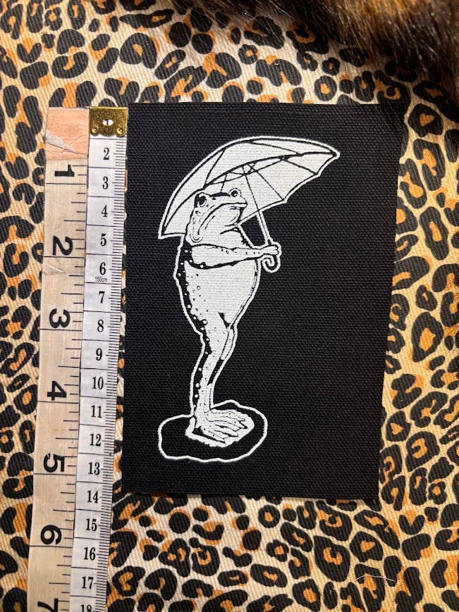 Sad frog holding an umbrella in the rain patch.