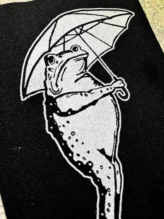 Sad frog holding an umbrella in the rain patch.